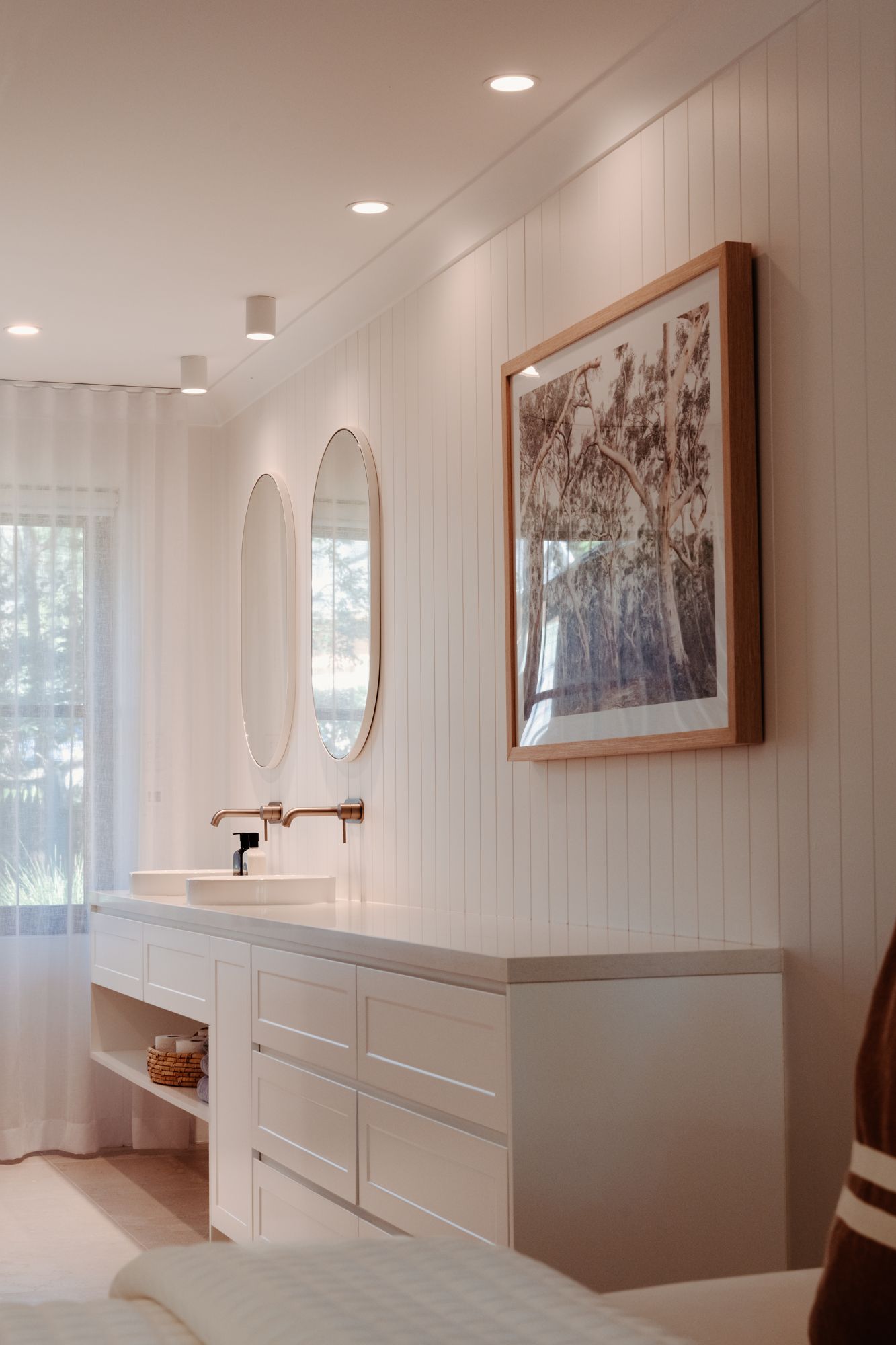 White bathroom with a double vanity, round mirrors and vertical panelled walls