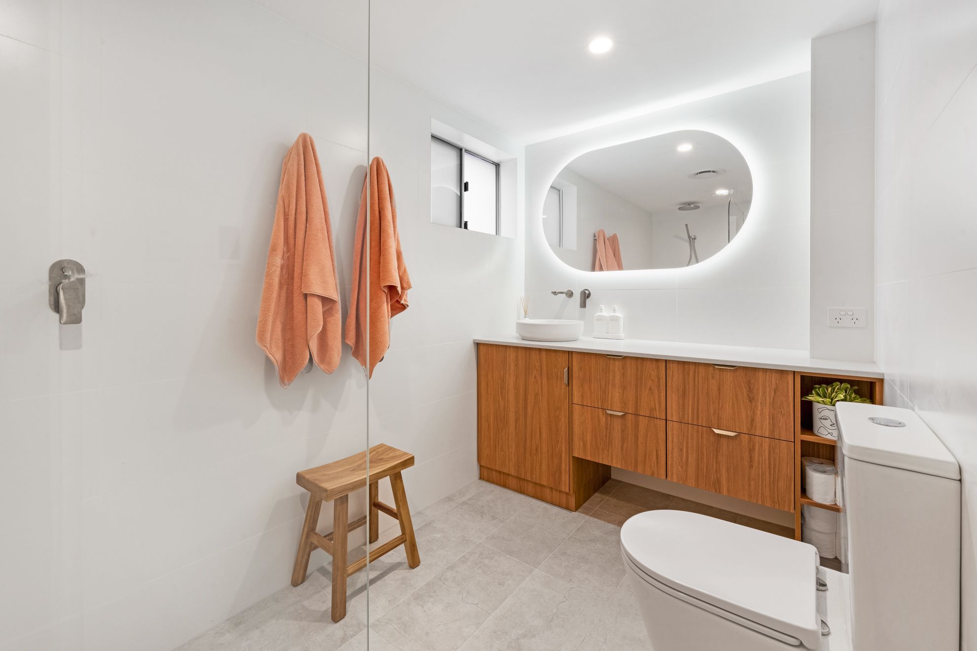 Renovated bathroom with a timber wall-hung vanity, oval backlit mirror and large pale floor tiles