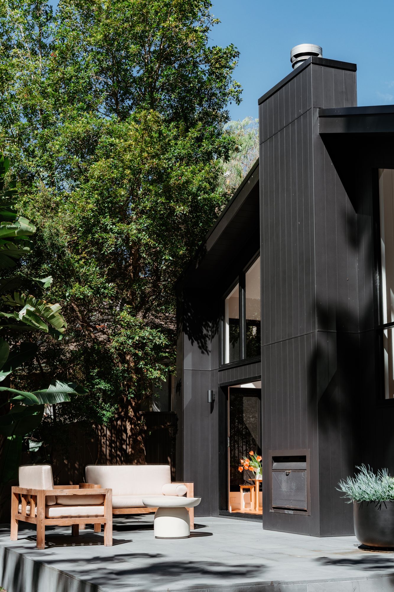 Tall home extension clad in black vertical boards, with an outdoor seating area in front