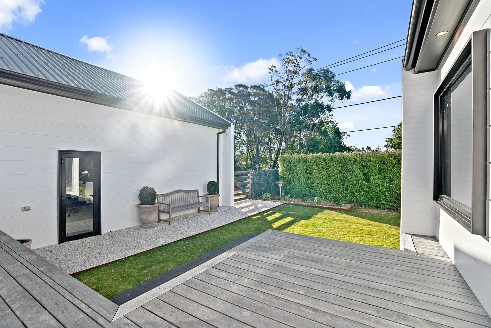 Timber courtyard deck wrapping a lawn beside a white rendered extension