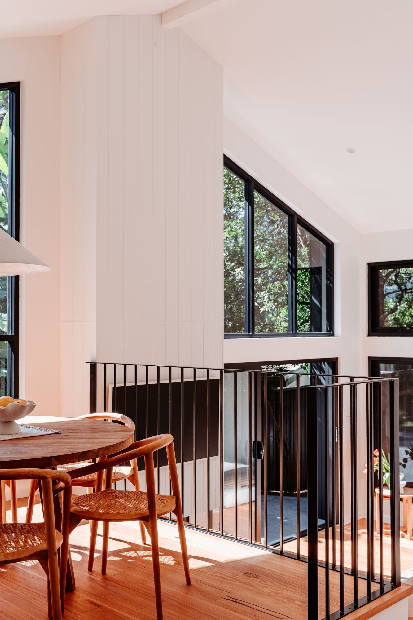 Light-filled dining area beneath a double-height void with a black steel balustrade