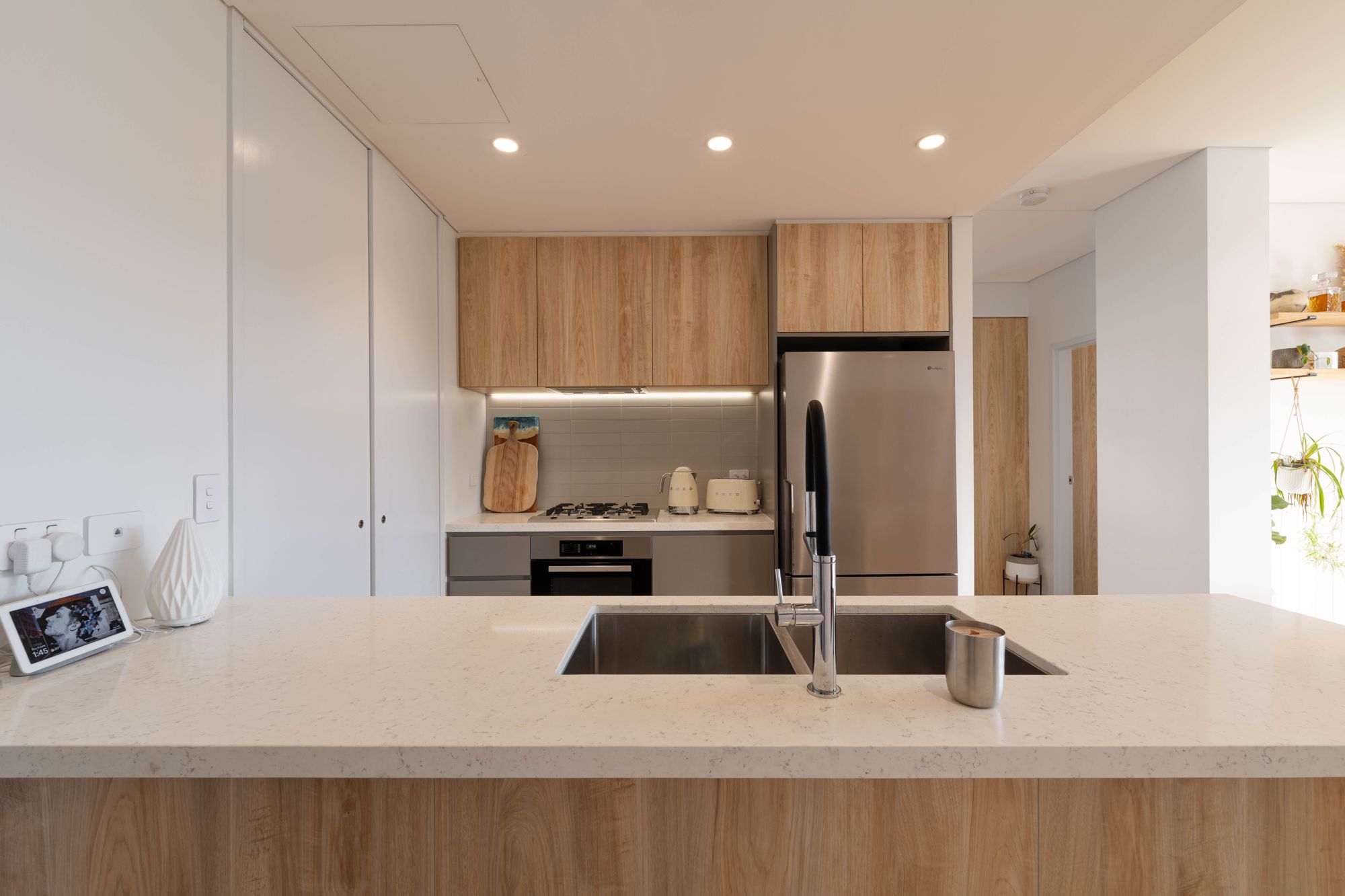 Modern kitchen with a stone island bench, timber-look overhead cupboards and built-in fridge