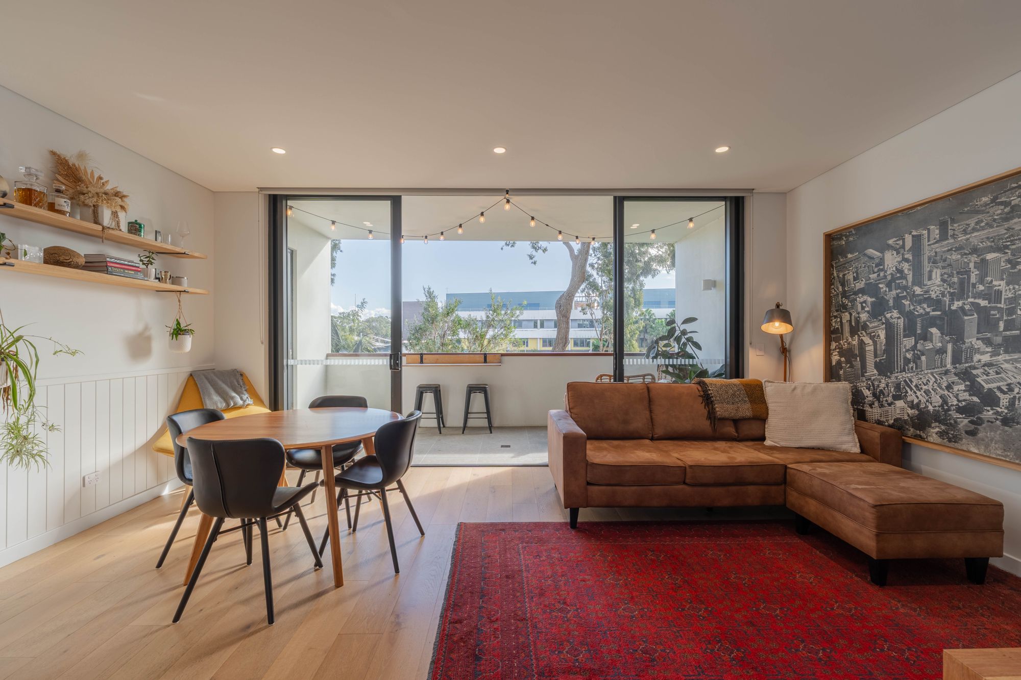 Open-plan living and dining room with timber floors, a leather sofa and sliding doors to a balcony