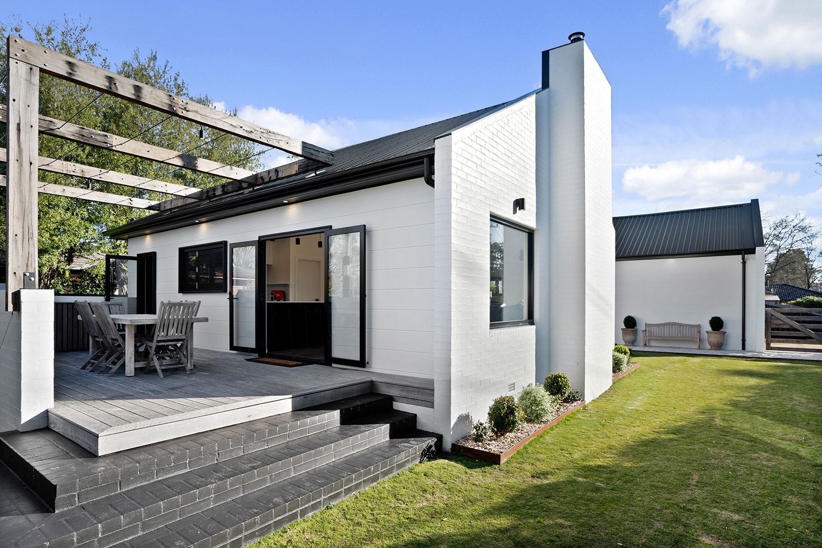 Rear extension in white painted brick with black-framed doors opening onto a new deck and pergola